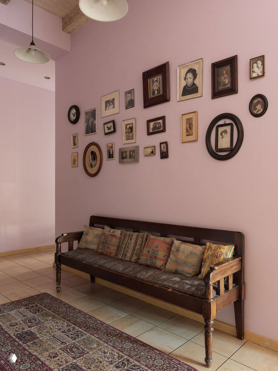 Пастельно‑розовая стена, композиция семейных фотографий и ретро‑скамья на переднем плане, тёплая и уютная прихожая или коридор в винтажном стиле.