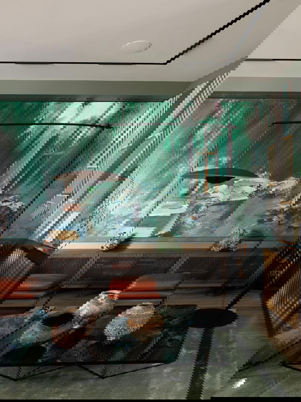 Просторный интерьер с крупной панорамной живописной работой в зелёных оттенках, низкой консолью, журнальным столом и декоративными керамическими сосудами.