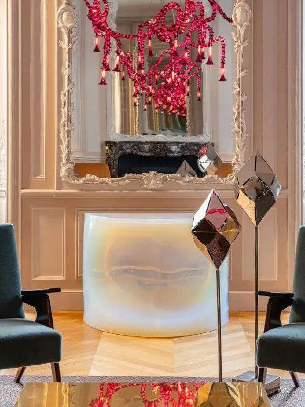 Отражающие геометрические скульптуры на стойках, перламутровая консоль и яркая розовая люстра в декоративной комнате Hôtel de Maisons — инсталляция на ярмарке.