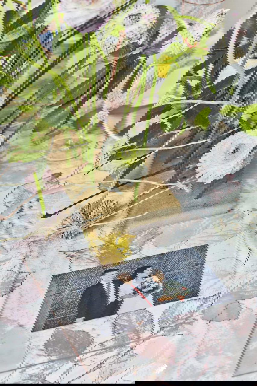 Фрагмент композиции с низкими цветочными инсталляциями и сухоцветами на столе; видны текстуры скатерти с принтом листьев и элементы натюрморта