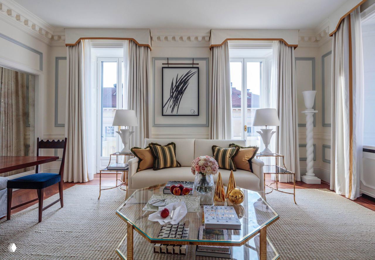 Гостиная номера в миланском отеле: светлый интерьер, софы и стеклянный журнальный стол с декоративными элементами и букетом цветов.