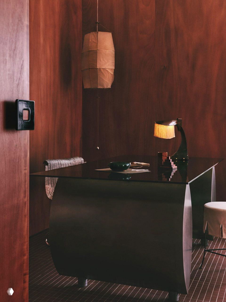 Рабочий кабинет с тёмным дизайнерским столом, подвесным светильником и деревянными панелями — гармония материалов и света.