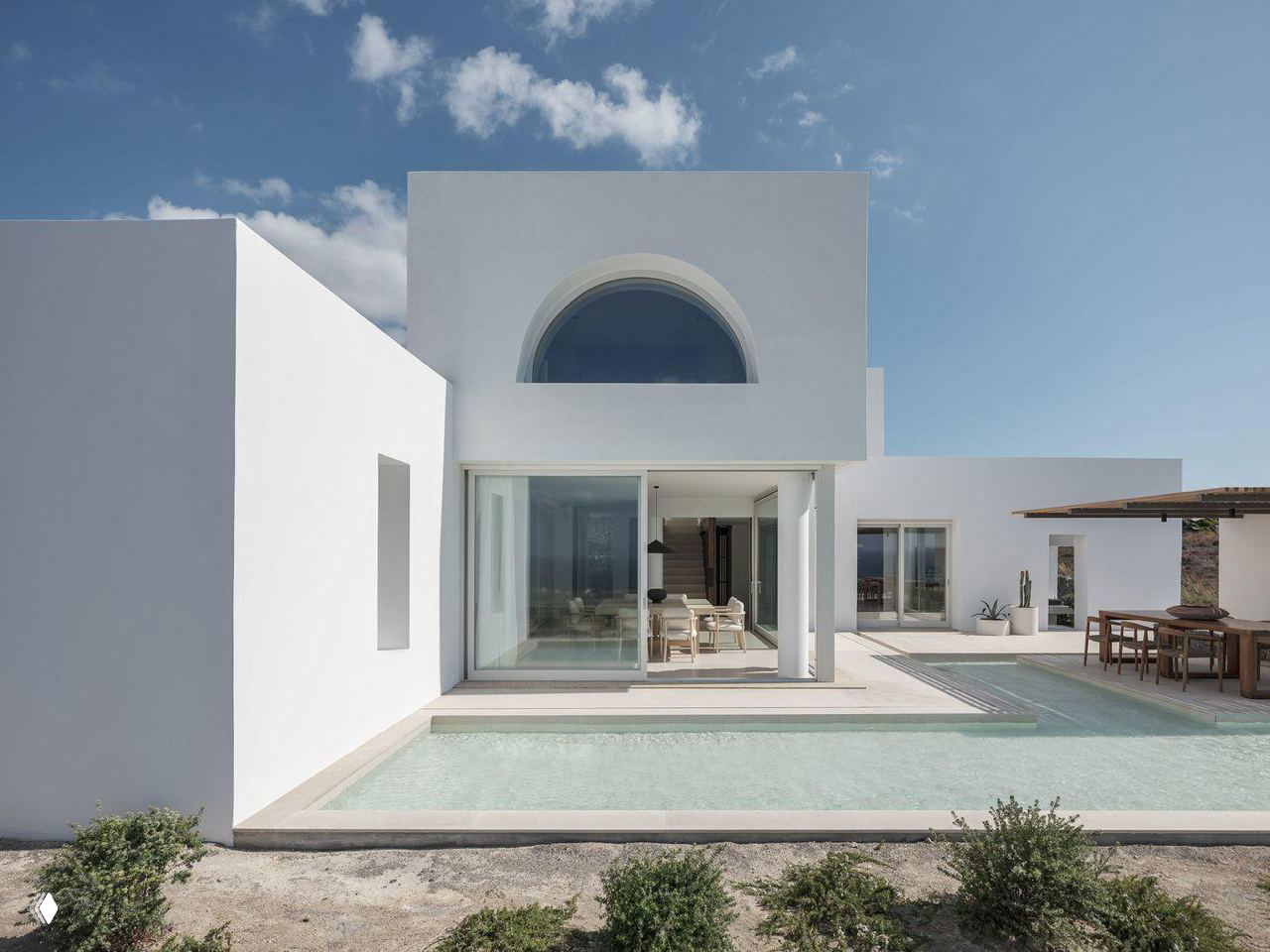 Патио и бассейн у главного фасада: прозрачные раздвижные стены, отражение неба и минималистская белая архитектура в кикладском стиле.