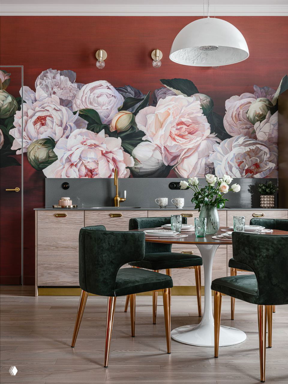 Яркая столовая зона и кухня без верхних шкафов на фоне крупного цветочного панно; мягкие темно-зеленые стулья и белый круглый стол в кадре.