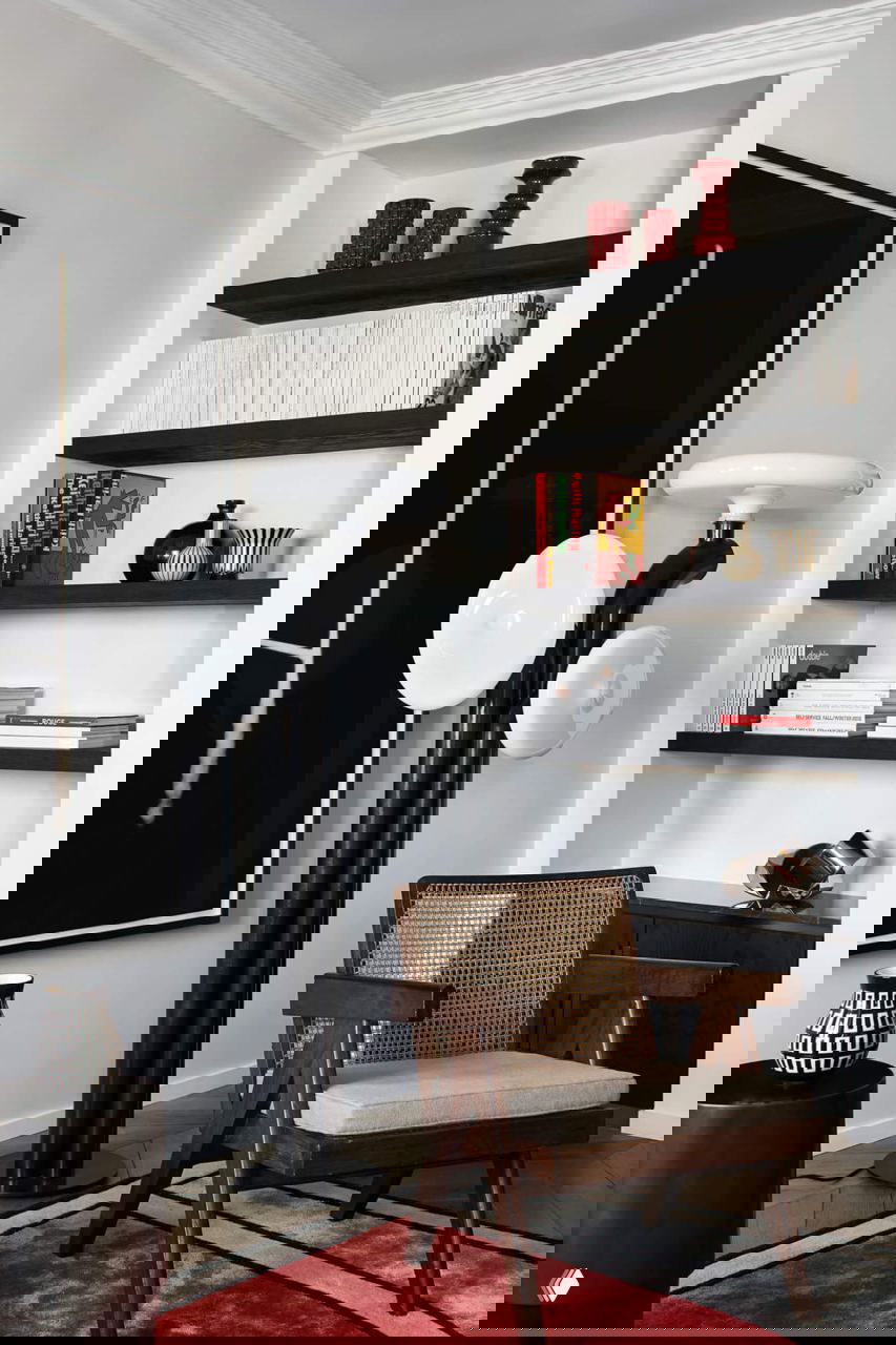 Уголок с деревянным креслом и встроенными полками, чёрно-белые акценты и яркий красный ковёр создают характерный интерьер для чтения.