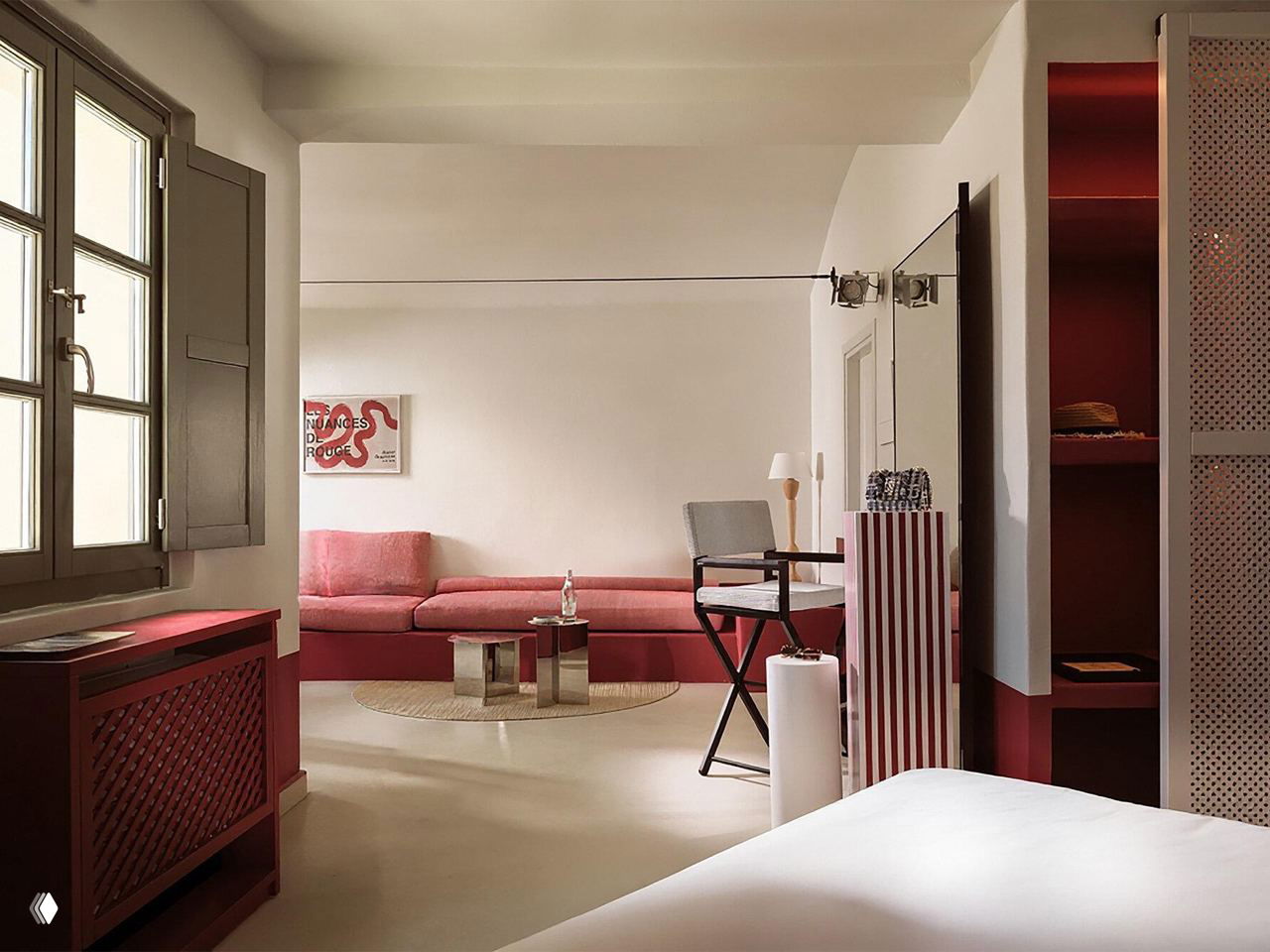 Гостиная зона номера с низким красным диваном, зеркальным столиком, большим окном и лаконичным бело‑красным интерьером в стиле Санторини