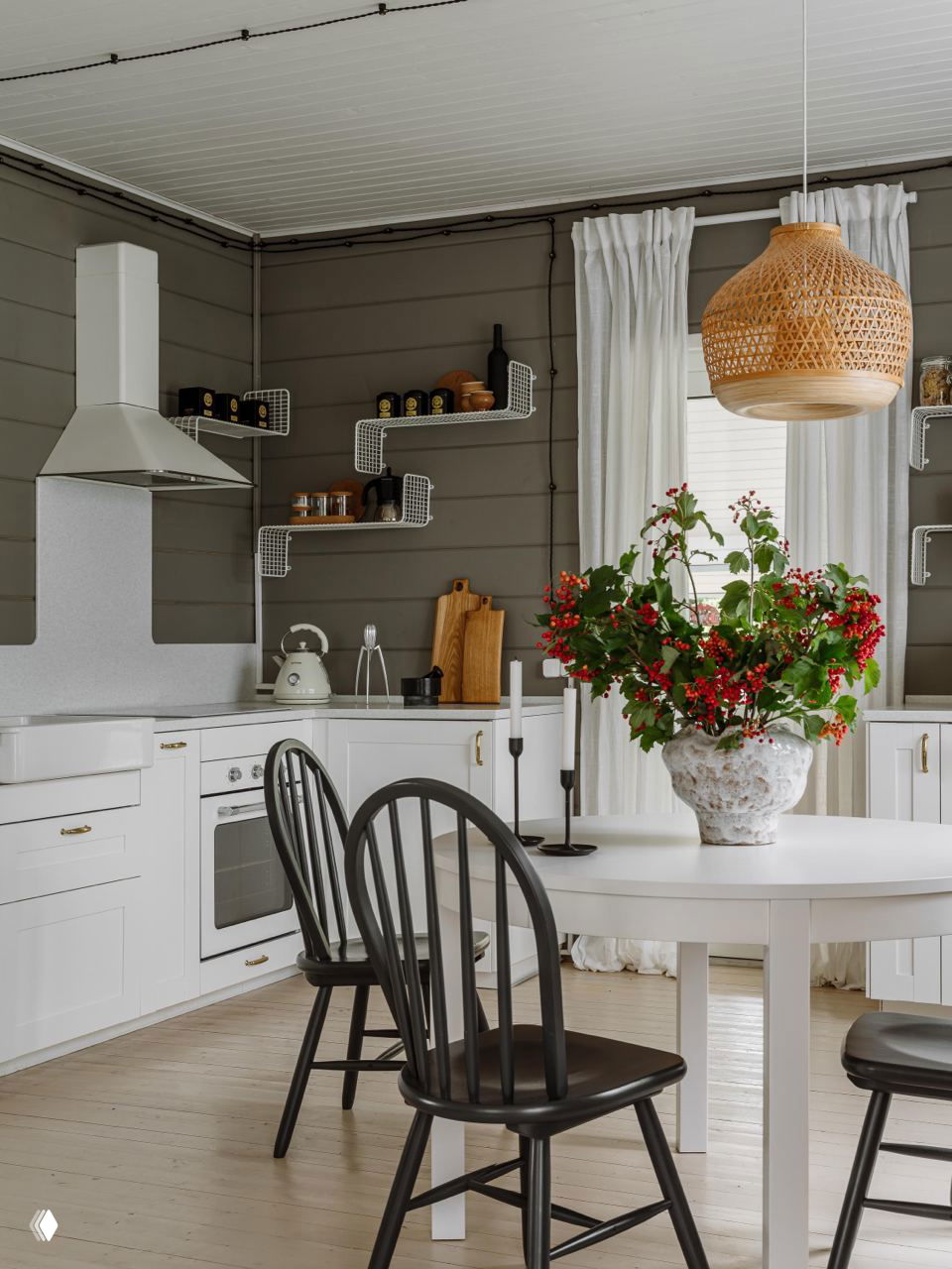 Кухня-столовая с белыми гарнитуром и круглым столом, плетеная подвесная лампа и ваза с букетом — воздушный скандинавский характер интерьера.