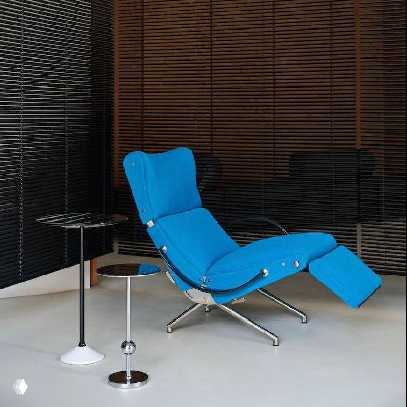 Ярко‑голубой шезлонг P40, дизайн Освальдо Борсани, в интерьерной сцене рядом с минималистичными столиками и темными жалюзи на фоне.