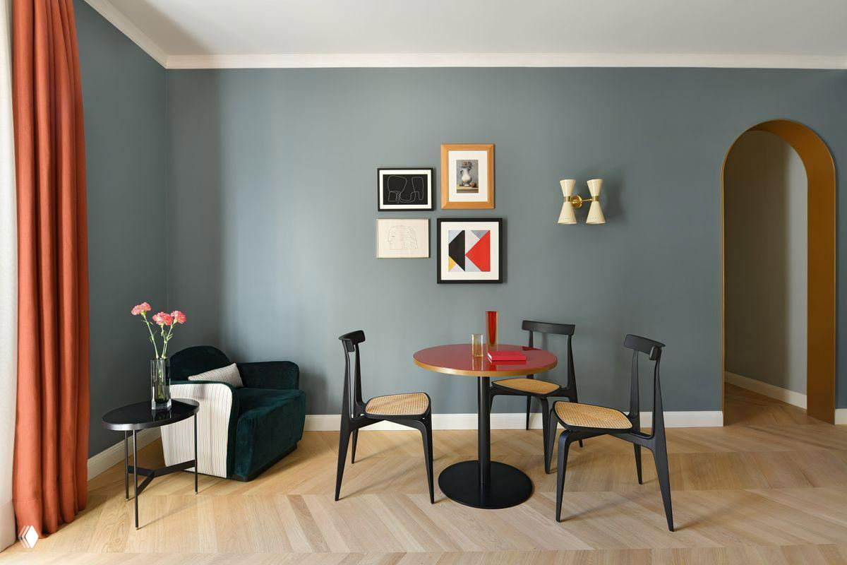 Минималистичная столовая зона в пастельных тонах: небольшая круглая столешница, четыре стула и декоративные изображения на стене.