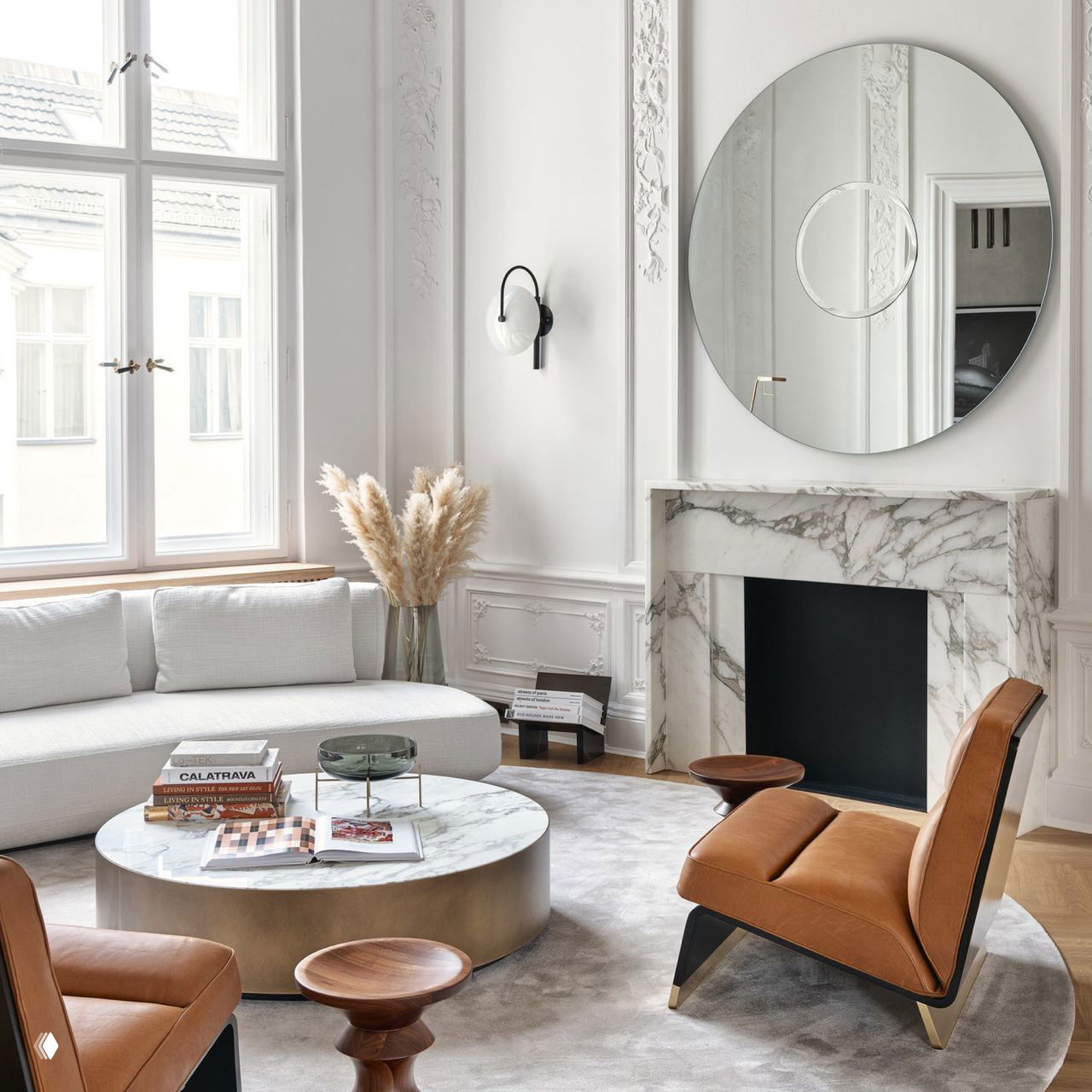 Светлая гостиная с большим круглым зеркалом и мраморным камином: небольшое настенное бра у зеркала создаёт локальный рассеянный свет.