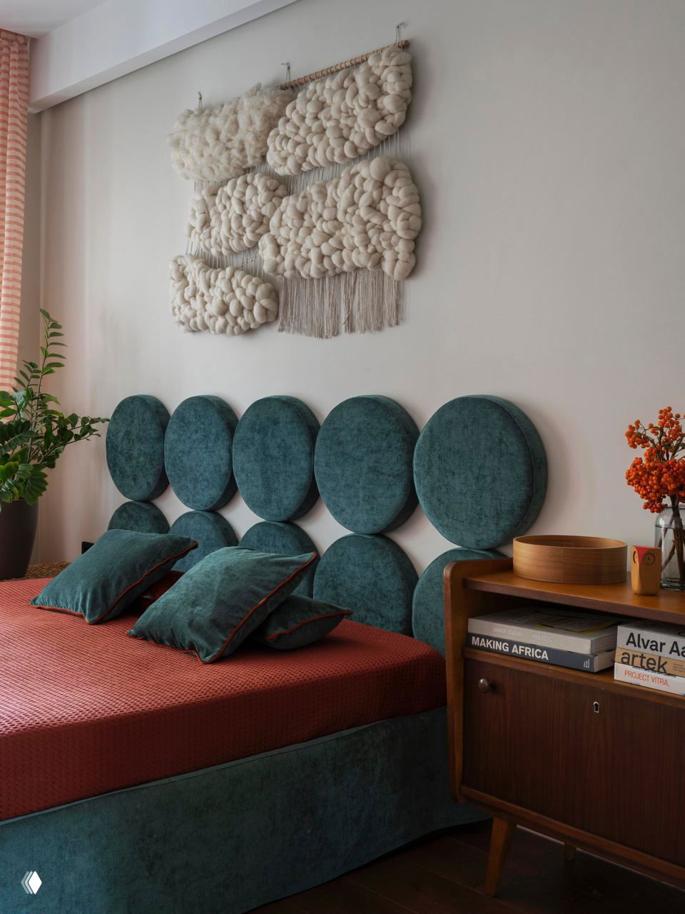 Спальня с крупным круглым бархатным изголовьем тёмно‑изумрудного цвета и большой текстурной панелью макраме над кроватью, уютный винтажный стиль.