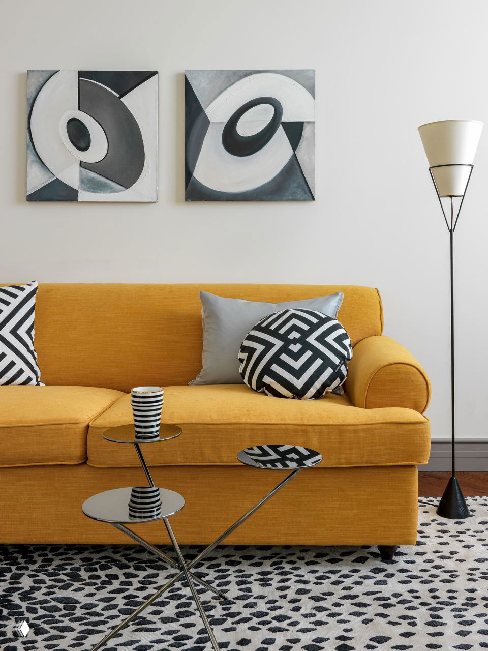 Жёлтый диван с чёрно‑белыми графичными подушками и небольшим журнальным столиком — контрастные принты в современной гостиной.