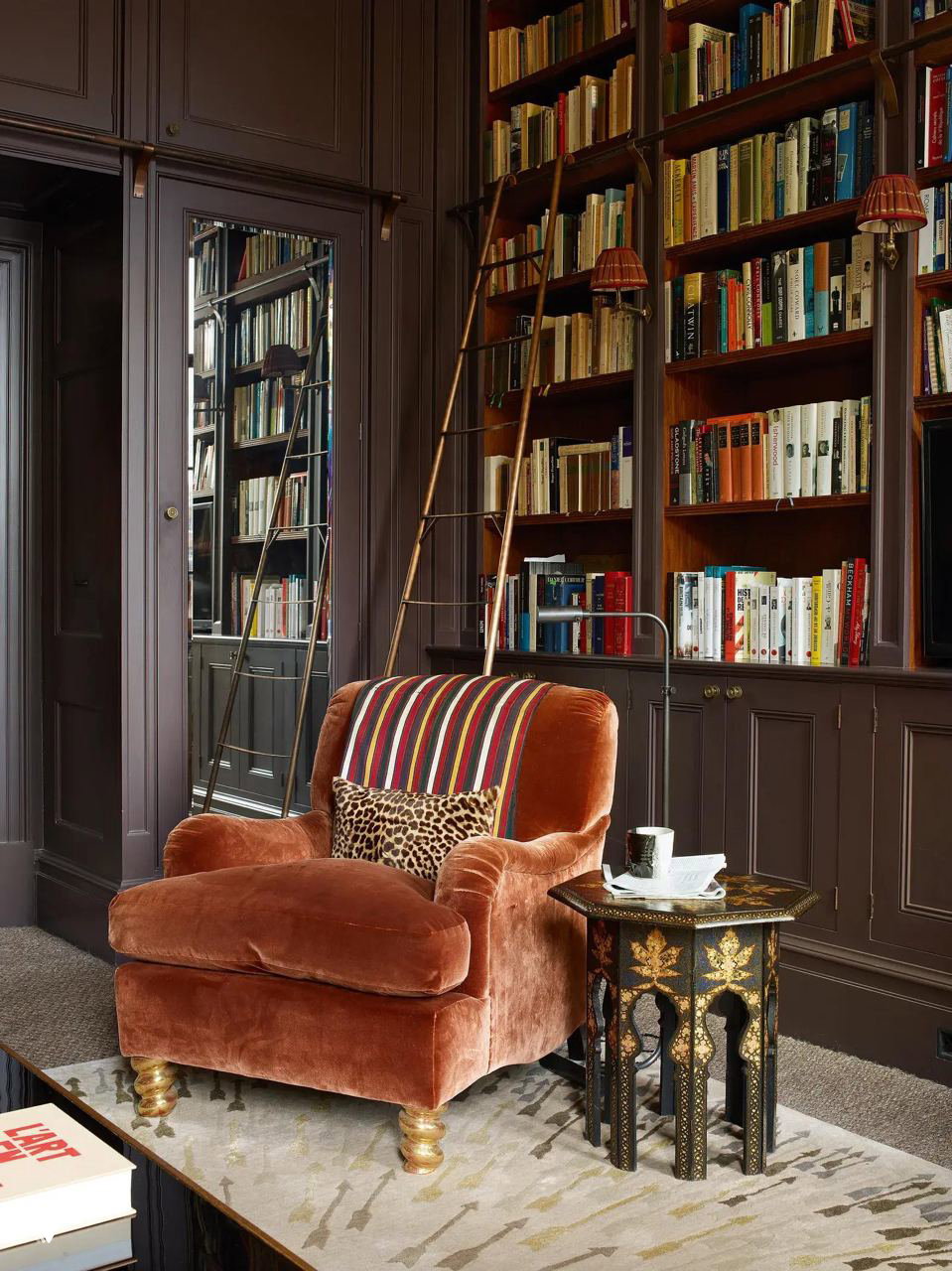 Библиотечный уголок с высоким книжным шкафом, телескопической лестницей и бархатным креслом — роскошная атмосфера для чтения.