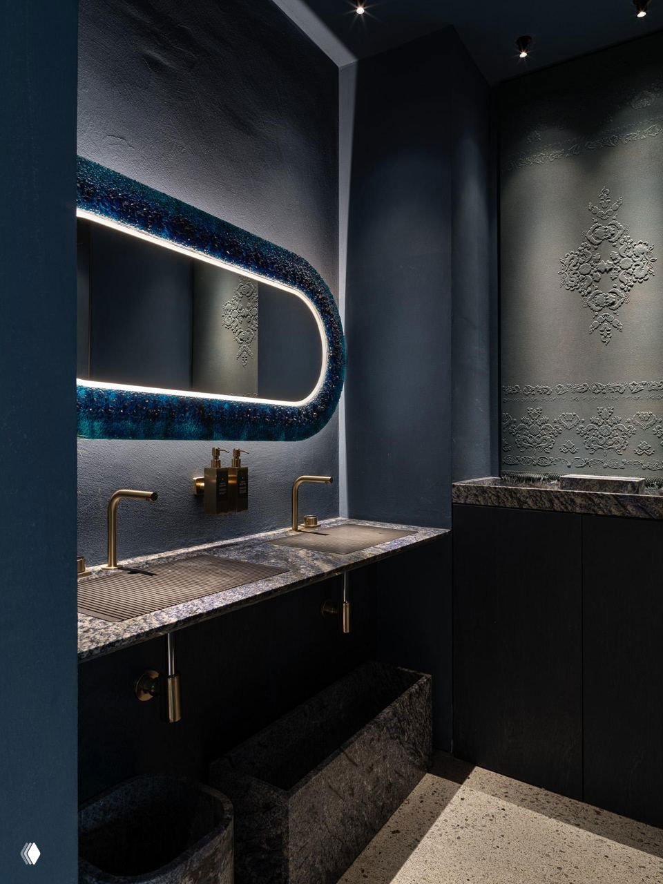 Фрагмент сервировки: тёмный деревянный стол с белой тарелкой, стеклом и салфеткой на фоне текстурной синей стены и аккуратного стула.