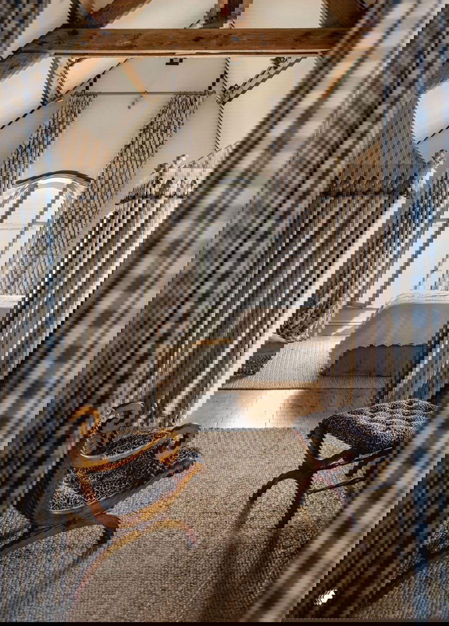 Проход в спальню с потолочными балками и парой полосатых палаток, используемых как декоративные ниши — игривое решение в интимной зоне дома.