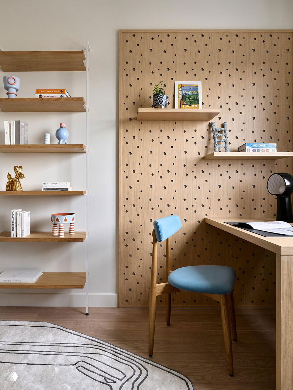 Рабочая зона с панелью перфорированного дерева, полками и деревянным столом; стул с голубой обивкой добавляет мягкий цветовой акцент.