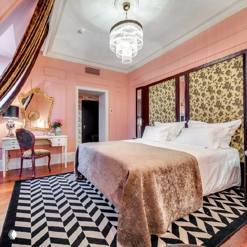 Номер с розовыми стенами, двуспальной кроватью, сверкающей хрустальной люстрой и графичным ковром — сочетание винтажных и современных деталей.