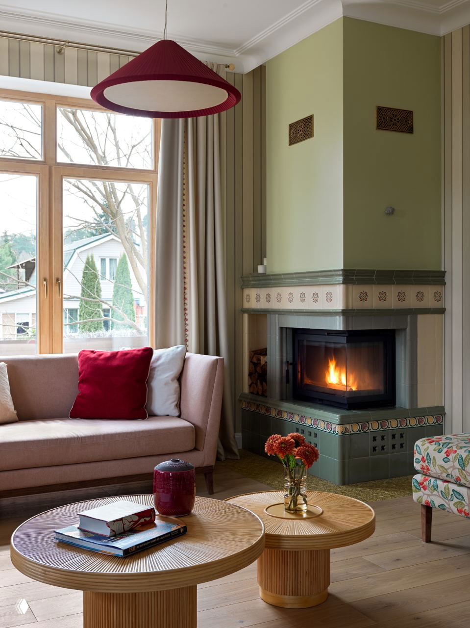 Гостиная с камином и оливково‑зелёными стенами, акцентной винной лампой и красной подушкой — теплое сочетание для жилой зоны.