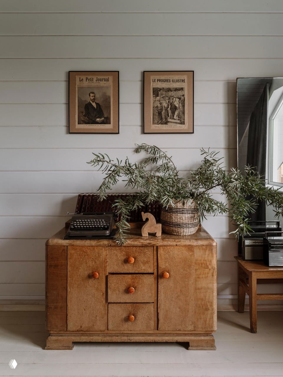 Деревянный комод с потертостями, старинная печатная машинка и зелёная ветка — колоритные античные акценты в интерьере дачи.