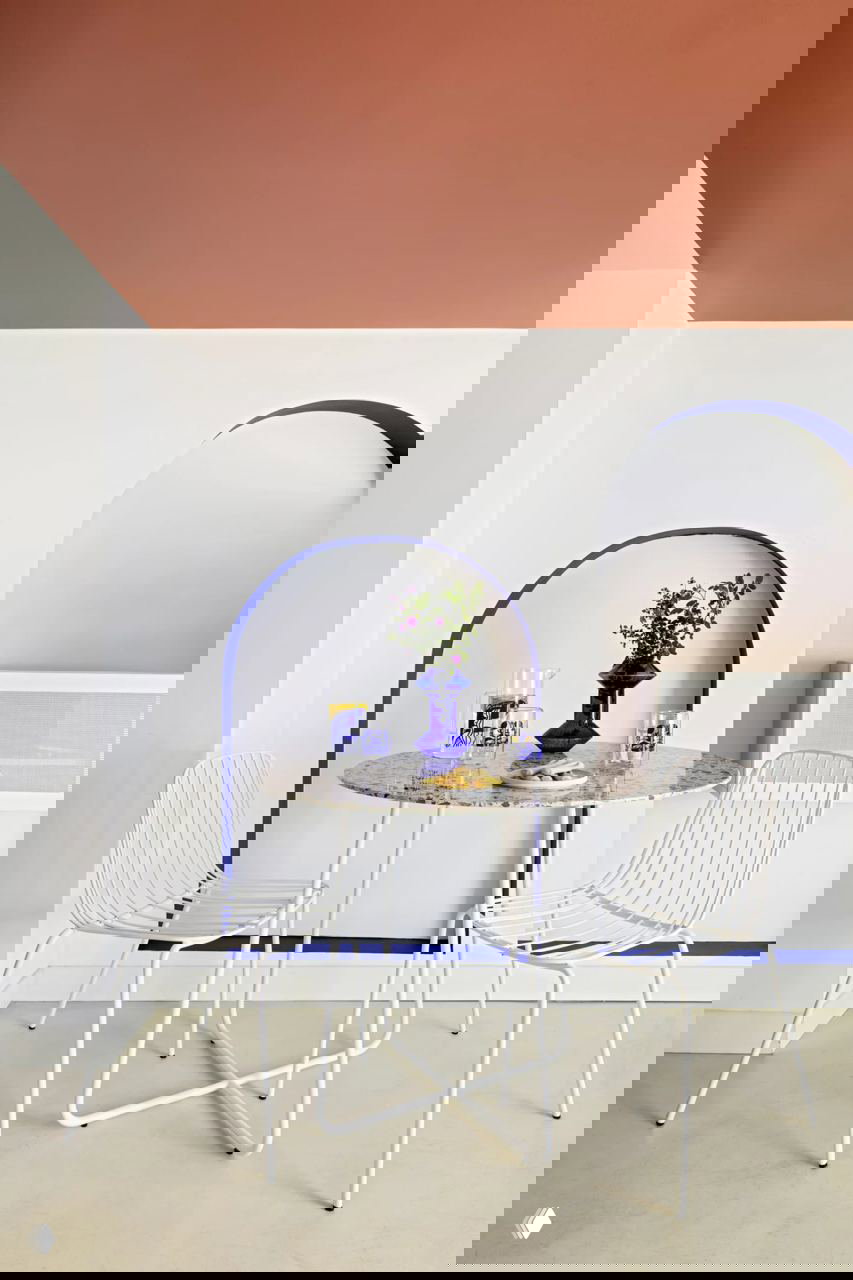 Небольшая столовая зона с круглым мраморным столом, белыми металлическими стульями и синими декоративными элементами в арочных нишах на стене.