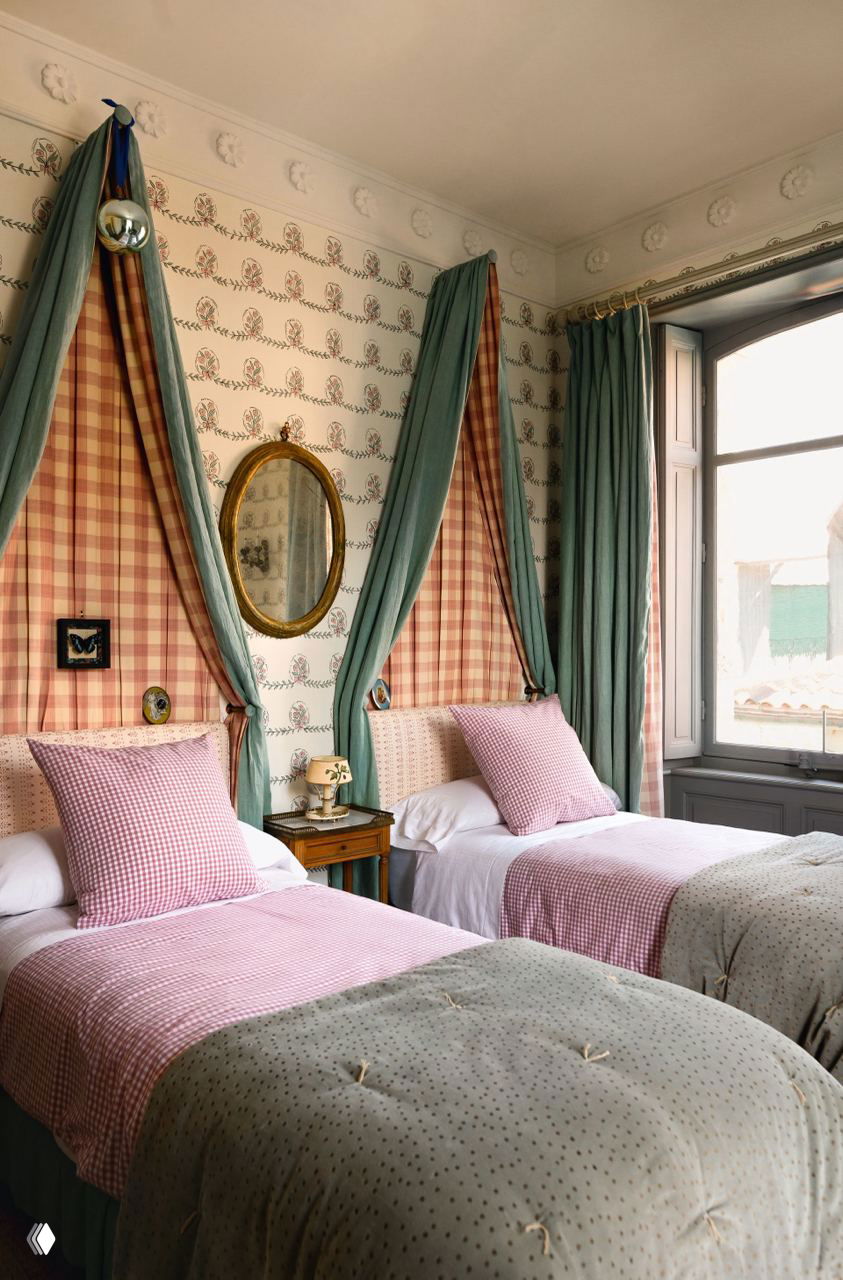 Две односпальные кровати с тканевыми балдахинами и клетчатыми драпировками над изголовьями, пастельные текстуры и классическая отделка комнаты.