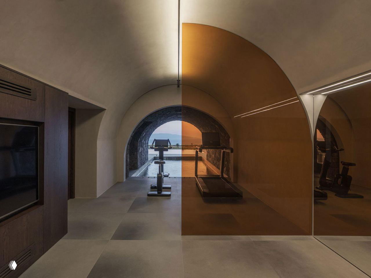 Подвальное помещение с тренажёрами: арочные своды, отражающие поверхности и бассейн, пронизывающий пространство до выхода к свету.