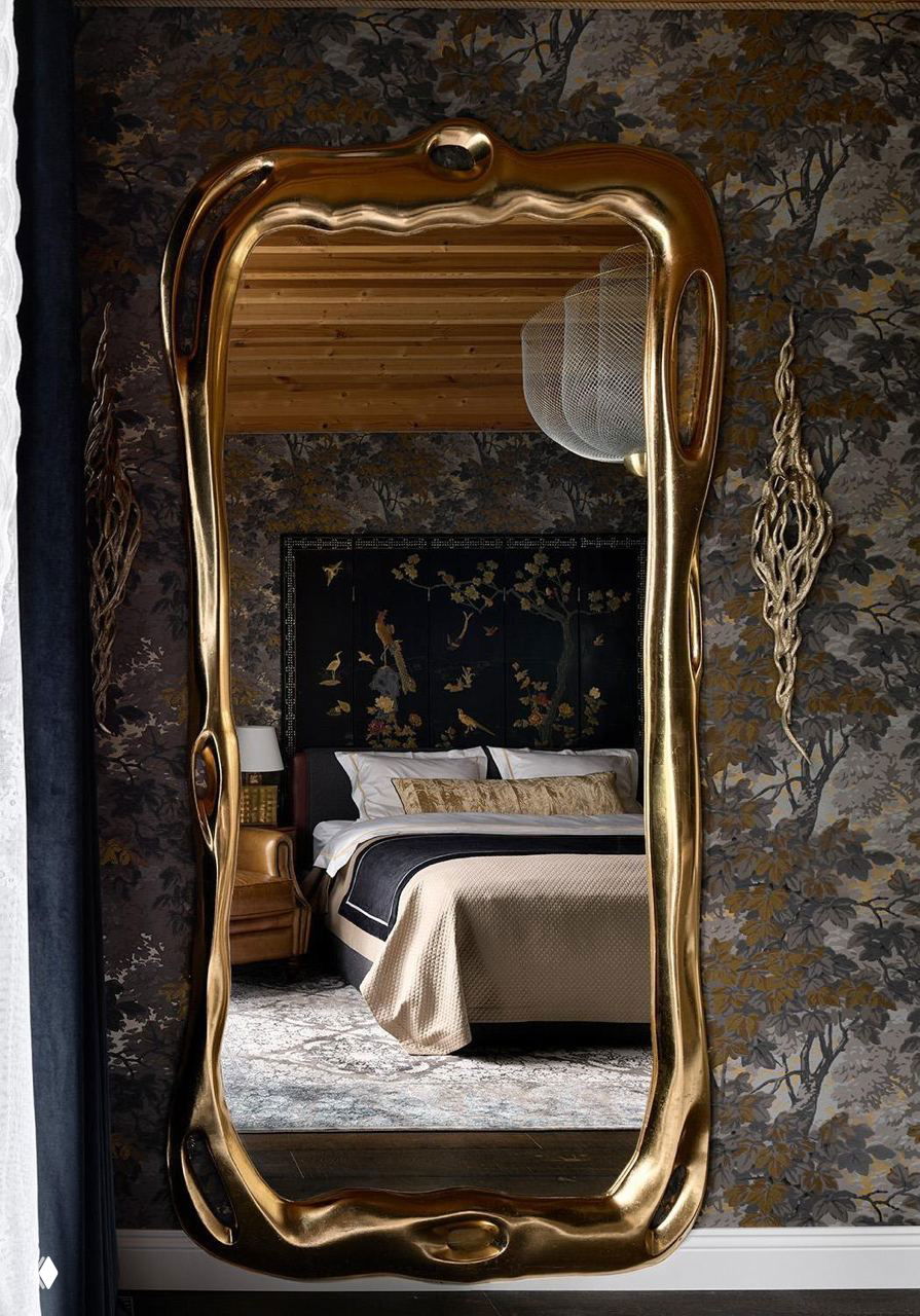 Фигурное золотое зеркало отражает спальню с тёмными обоями и классической мебелью — винтажные акценты в доме в Подмосковье.