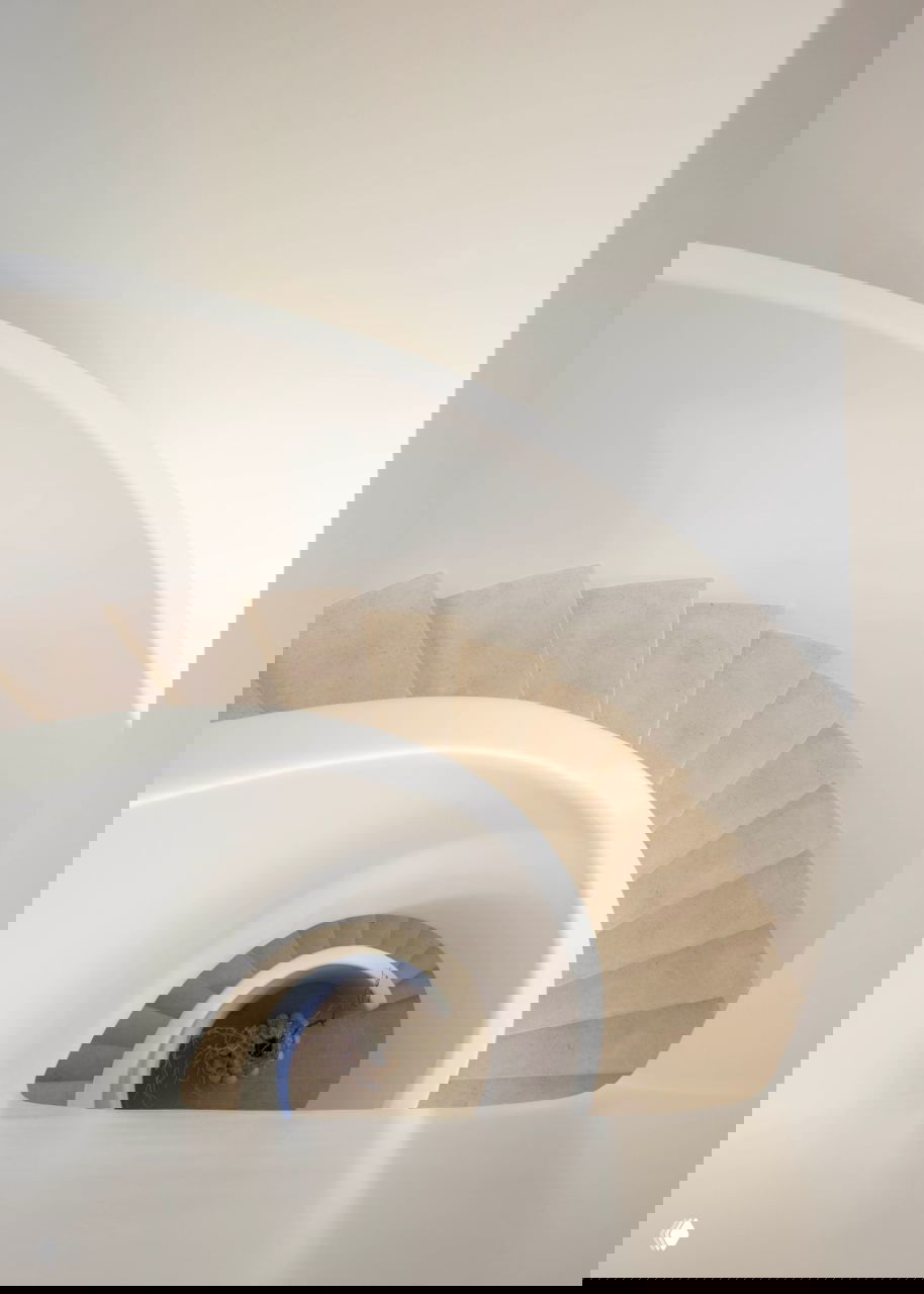 Вид сверху на спиральную лестницу — органичная форма ленты и ступени из светлого камня, геометрия и тени в центре.