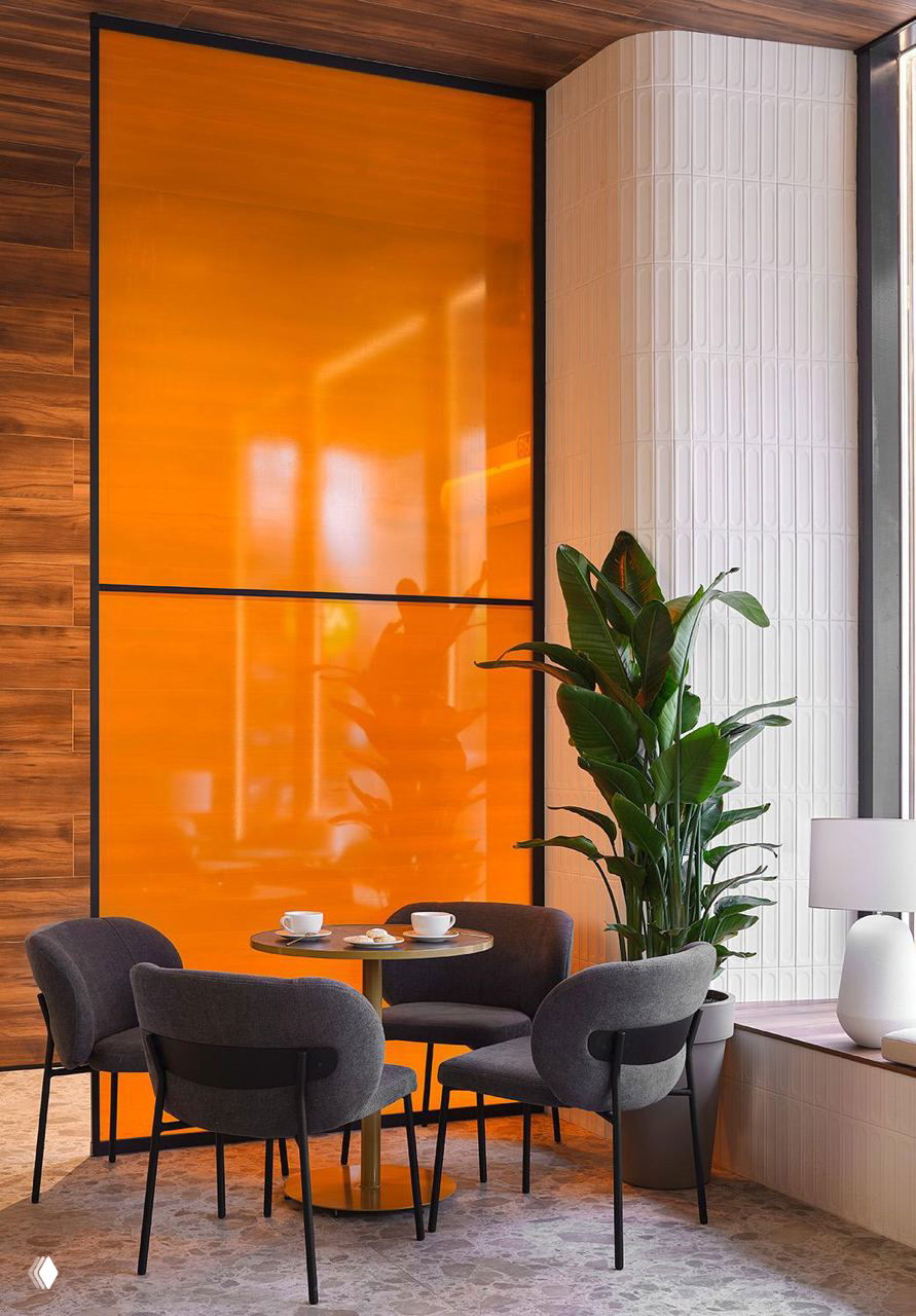 Уютный столик у окна в ANY Coffee Spot: небольшая посадочная группа, яркая оранжевая панель и высокое растение в горшке у витрины.