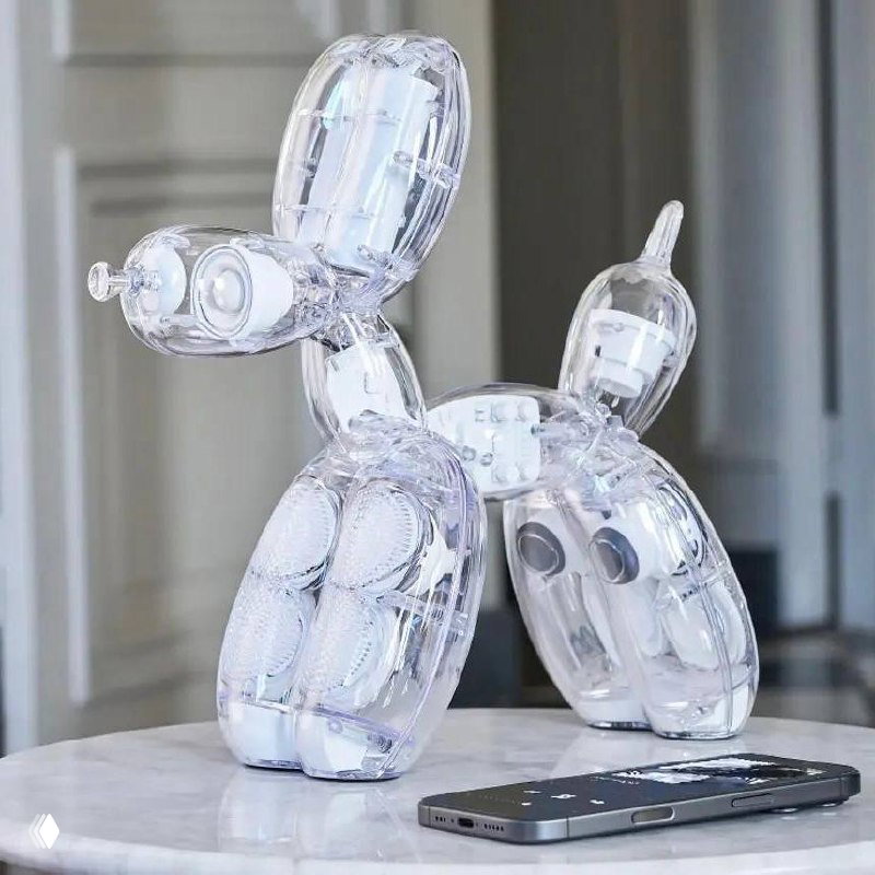 Прозрачная колонка Balloon Dog с белыми динамиками на мраморной поверхности рядом с смартфоном, демонстрирующая масштаб и подключение к устройству.