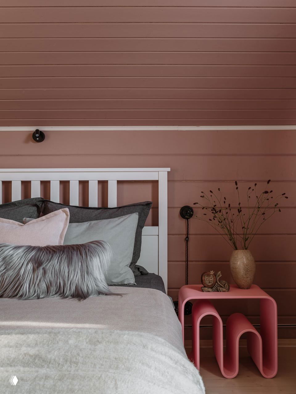 Спальня с розовым настенным и потолочным покрытием, кровать с многослойными текстурами и декоративной подушкой — мягкая, уютная атмосфера.
