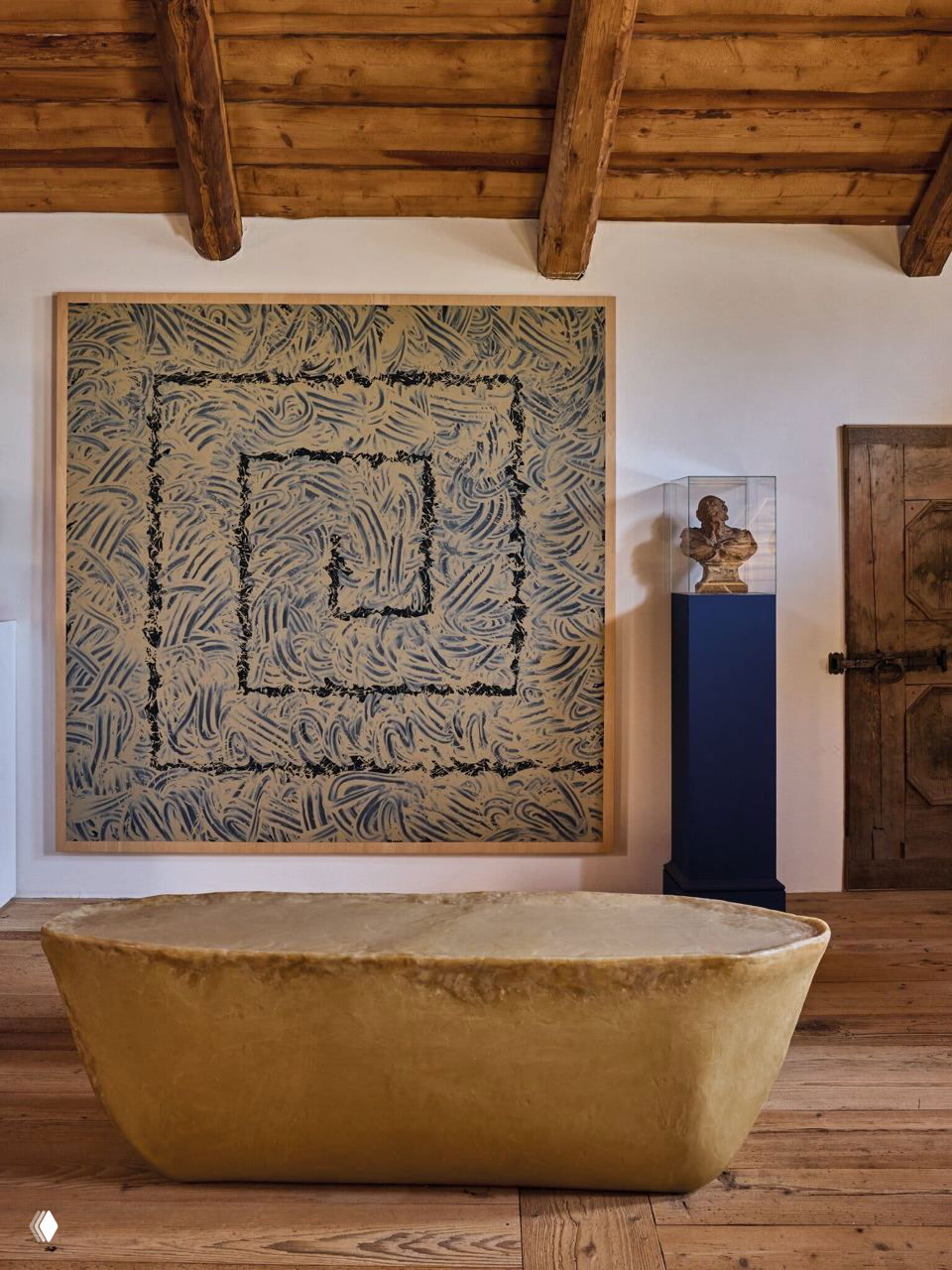 Интерьер с крупной абстрактной картиной и каменным предметом-пуфом на переднем плане; натуральные материалы и текстура дерева доминируют в пространстве.