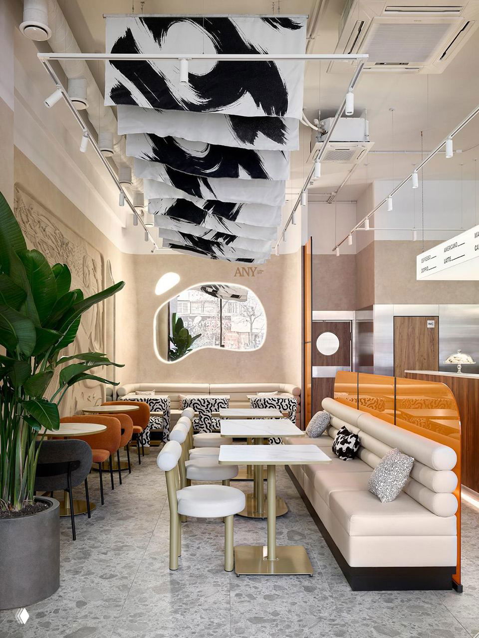 Общий вид помещения ANY Coffee Spot: ряд столиков и диванов, подвесные полотнища с монохромными мазками и светлая палитра материалов и фактур.