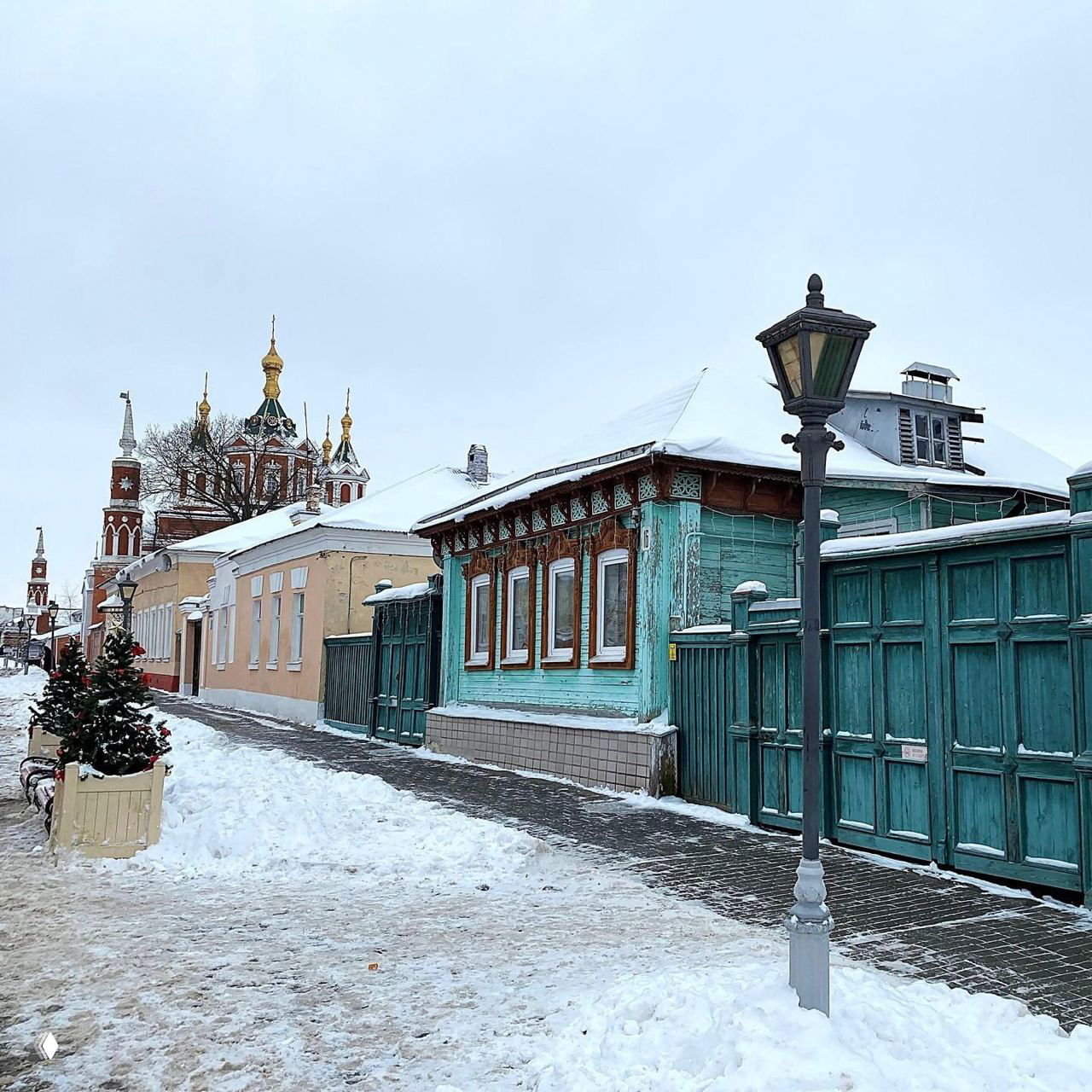 Улица старого города зимой: деревянные дома с резными наличниками, снежная тротуарная дорожка, фонарный столб и тихая атмосфера.
