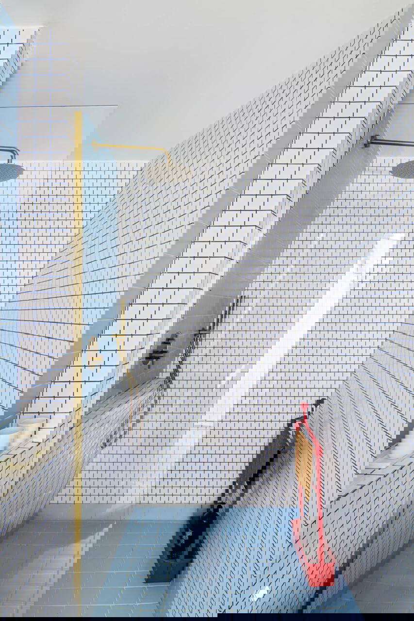 Маленькая душевая кабина в белой сетчатой плитке и нежно-голубой поддоном; аккуратный золотой душ и минималистичная организация пространства.