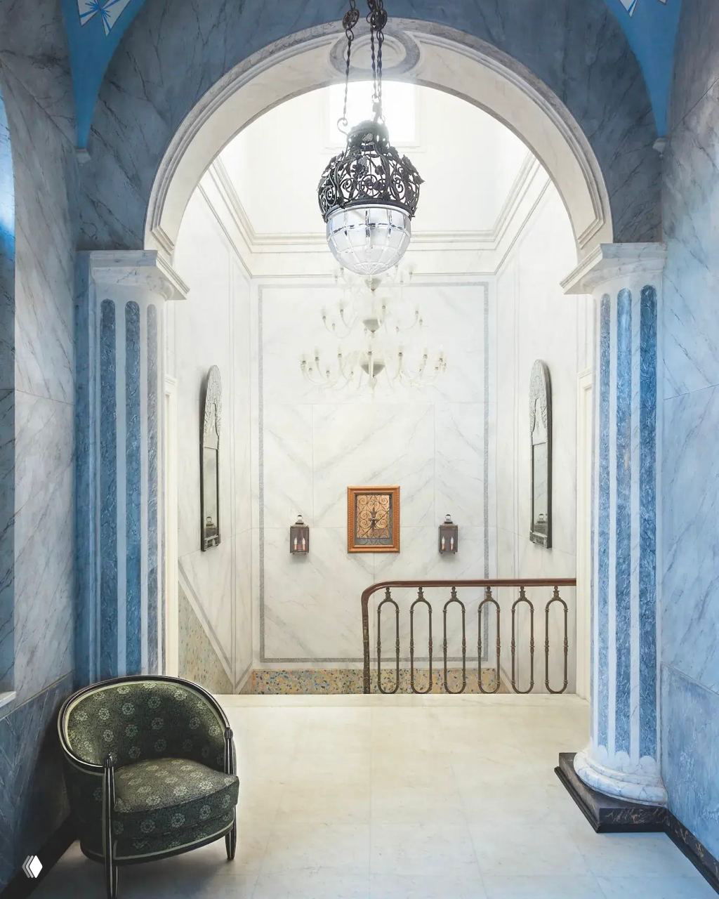 Парадная прихожая с арочным проёмом в неоклассическом стиле: мраморные панели, подвесная люстра и голубые декоративные полосы для выразительности интерьера.