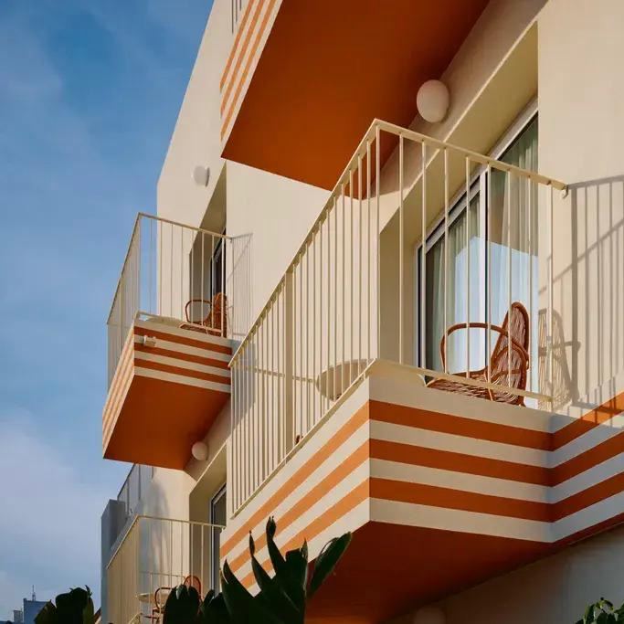 Балконы и террасы Riviera с бело‑оранжевыми полосами: вид на маленький балкон с креслом и характерный ретро‑настрой 1970‑х.