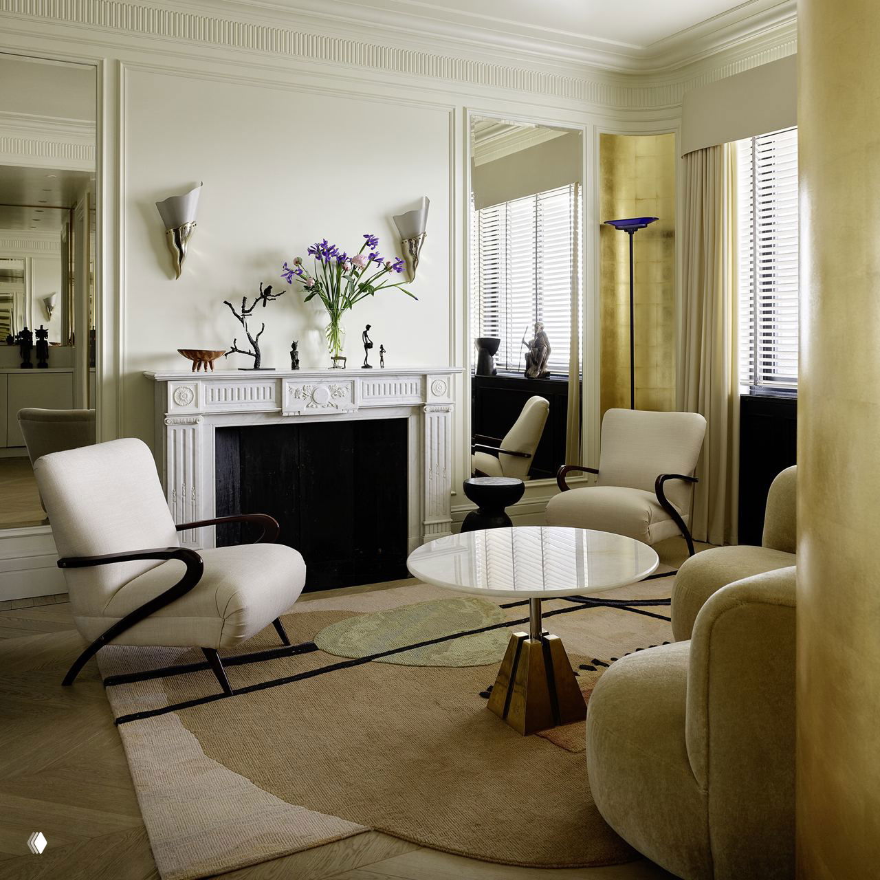 Классическая гостиная с белым камином, парой кресел и декоративными бра на стене — уютный уголок для чтения и бесед.