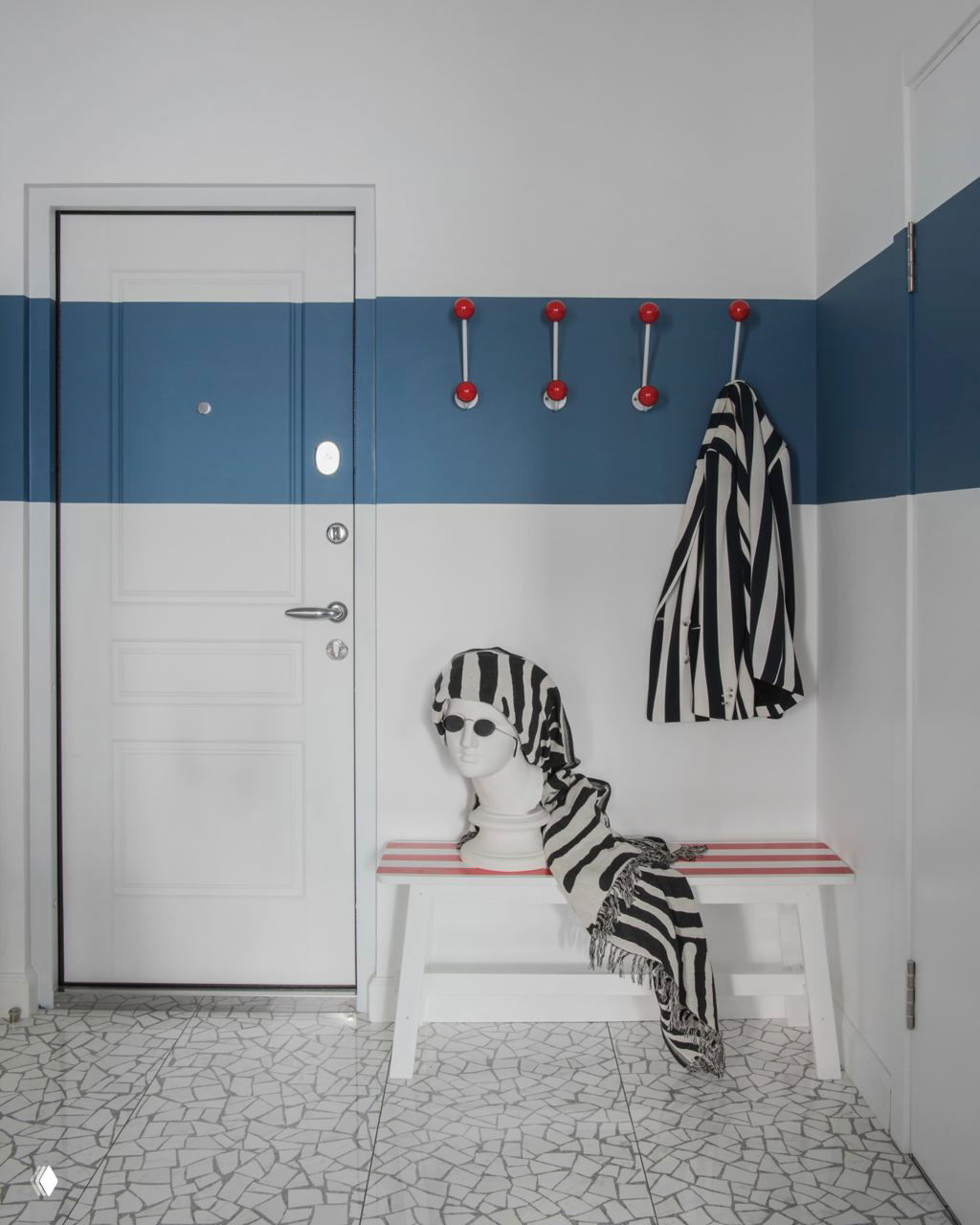 Минималистичная зона у входа с широкой голубой полосой на стене, рядом крючки для верхней одежды, скамья и стилизованный манекен с полосатым шарфом — дизайнерский акцент.