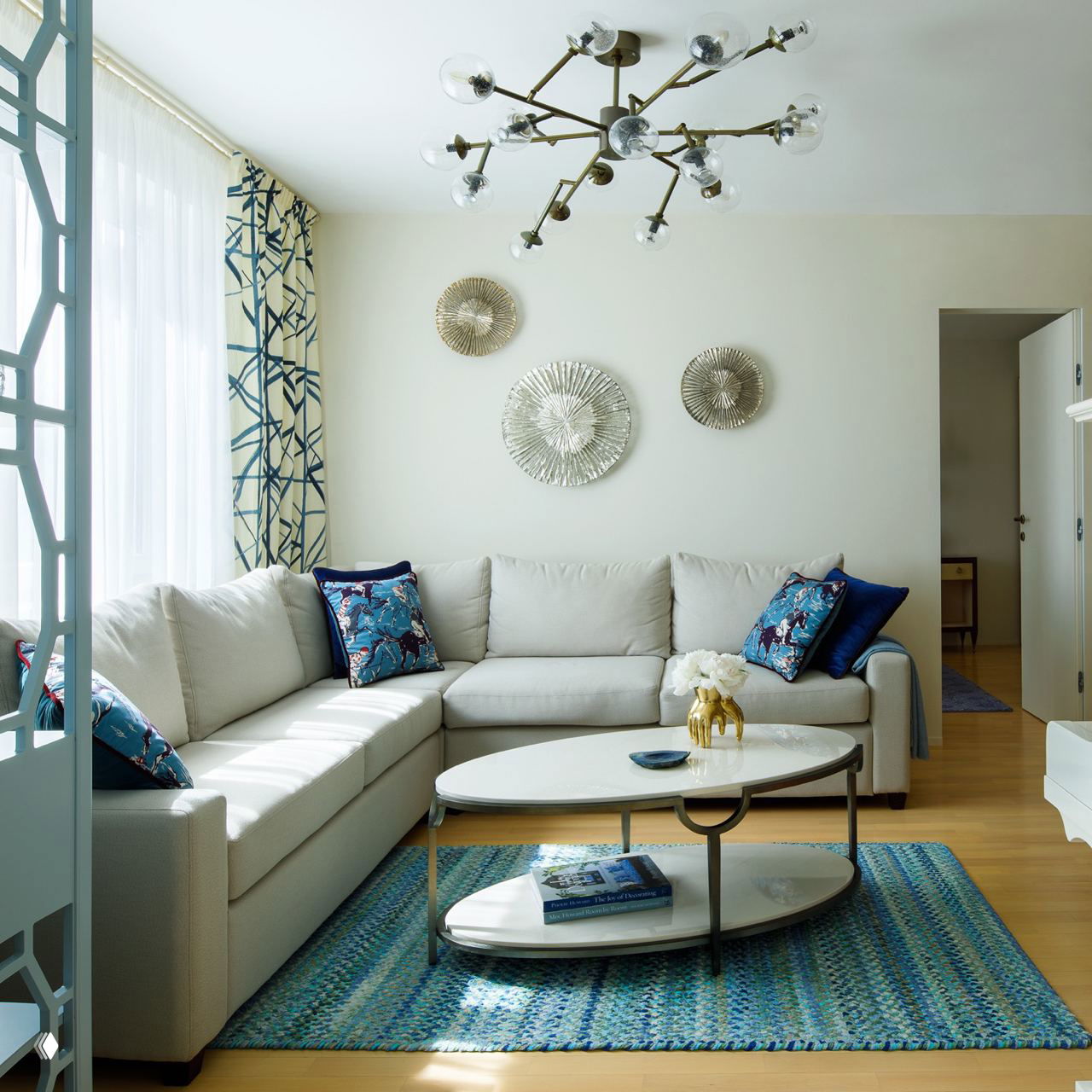 Современная гостиная с большим угловым диваном и бронзовыми декоративными элементами; бра отсутствуют в центре, но показывают зонирование стен.