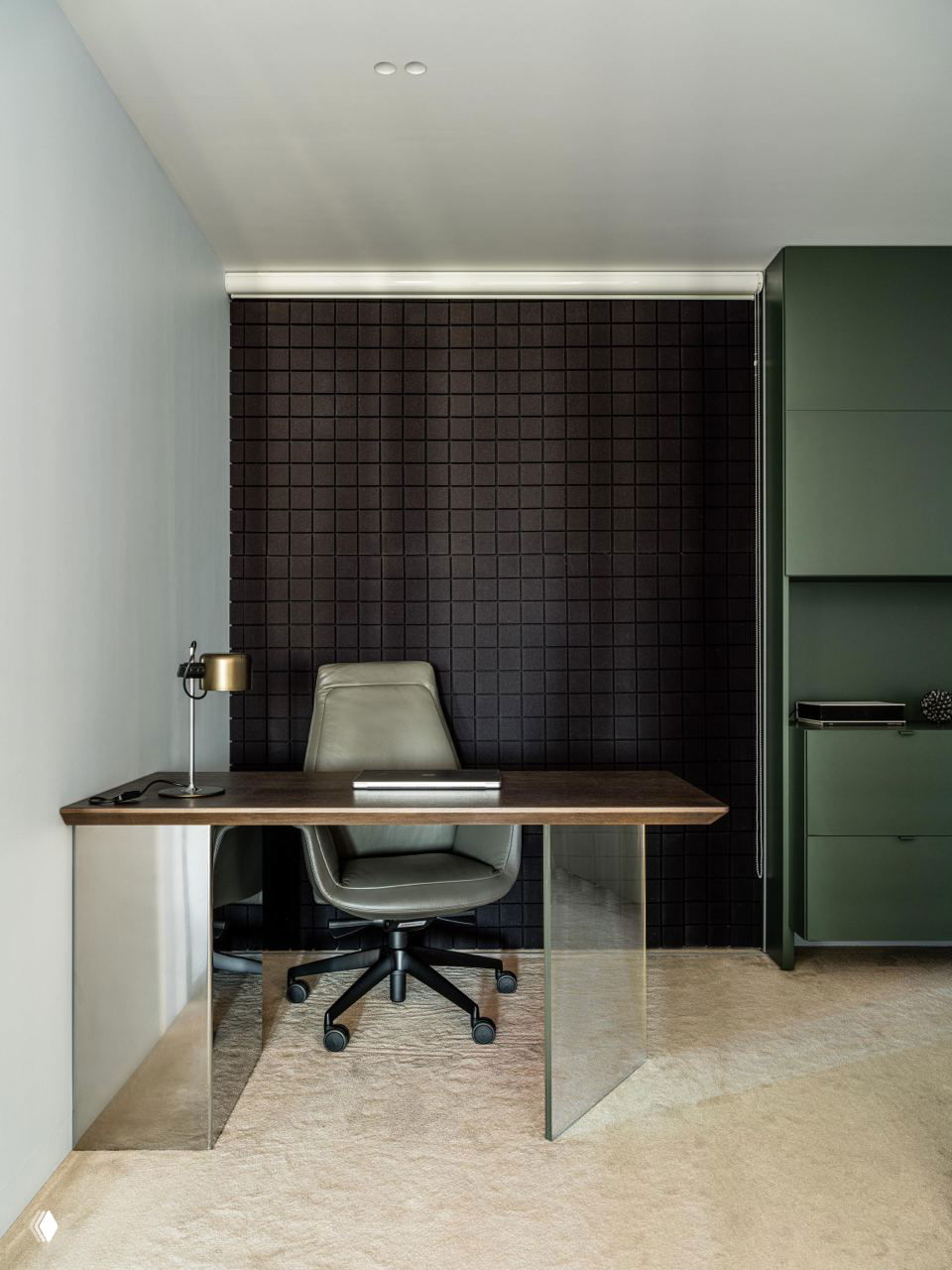 Отдельный кабинет-студия: деревянный стол с прозрачными опорами, кожаное кресло на колёсиках и тёмная звукопоглощающая панель на стене позади.