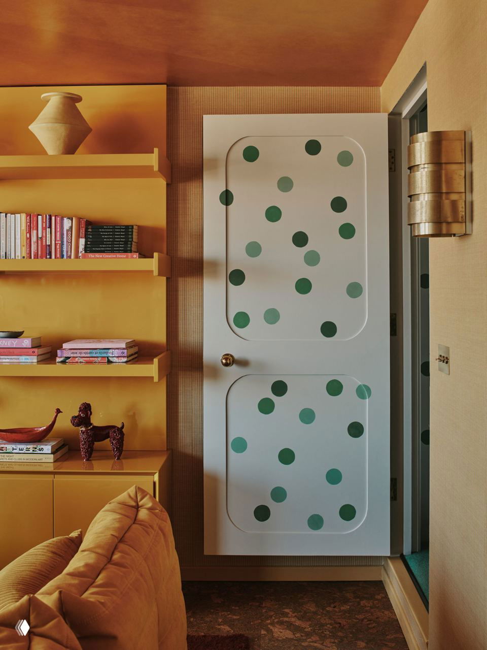 Дверь, расписанная зелёными горошинами, на фоне жёлтой мебели и полок — декоративный приём в интерьере, отсылающий к эстетике 1960-х годов.