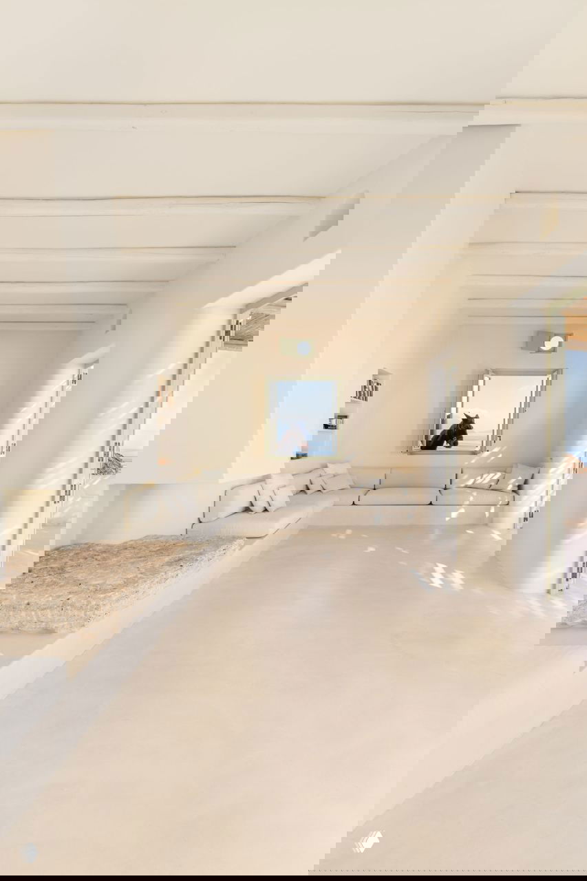 Просторная светлая гостиная с встроенным низким диваном, большими окнами и мягким естественным освещением — атмосфера спокойствия и медитации.