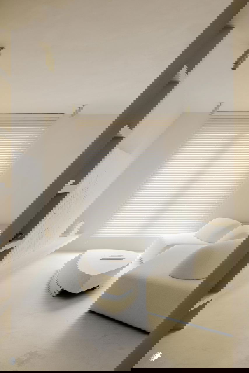 Нежная световая композиция у окна: низкий кофейный стол и мягкий модульный диван на фоне высоких жалюзи и ровной светлой отделки.