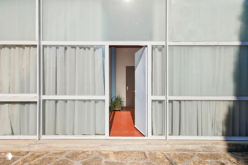 Фасад и вход виллы — крупные остекленные панели, частично матовое стекло и открытая дверь; архитектура 1930-х годов по проекту Ле Корбюзье на холме в Провансе.