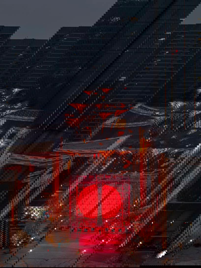 Вид вблизи на вход в инсталляцию DIVIDED: две светящиеся красные полусферы в металлической конструкции на городской площади вечером.