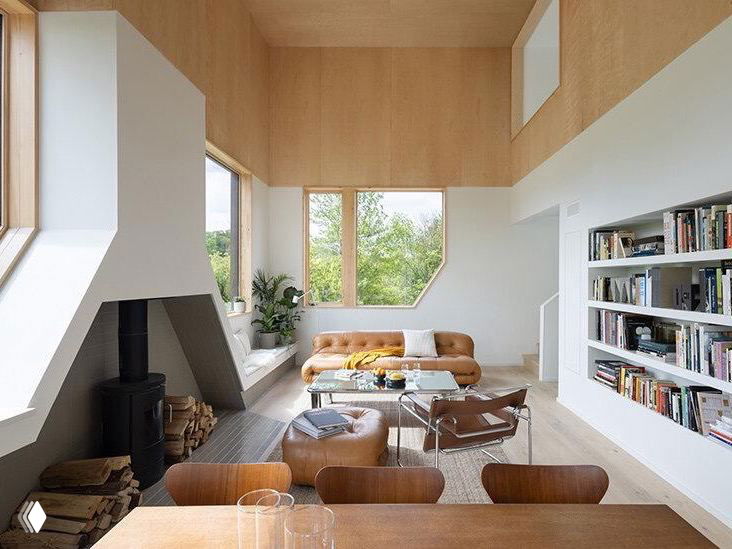 Кухня-столовая в светлых тонах: деревянная мебель, стол для обедов и рабочая поверхность у окна с видом на зелень вокруг дома.