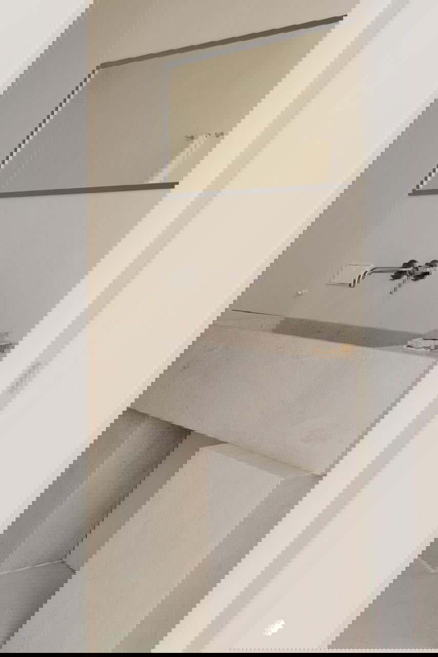 Умывальник из травертина и настенный сантехнический смеситель: монохромный каменный стол-раковина в сдержанном дизайне ванной комнаты.