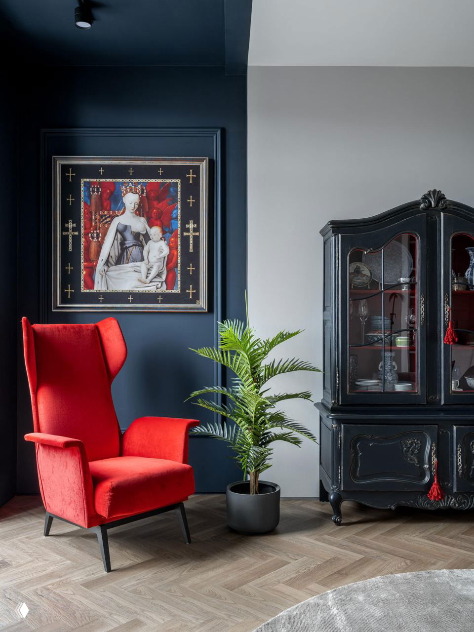 Уютный уголок гостиной: красное кресло в стиле, чёрный винтажный сервант и декоративная картина на фоне тёмно-синей стены, текстура паркета.