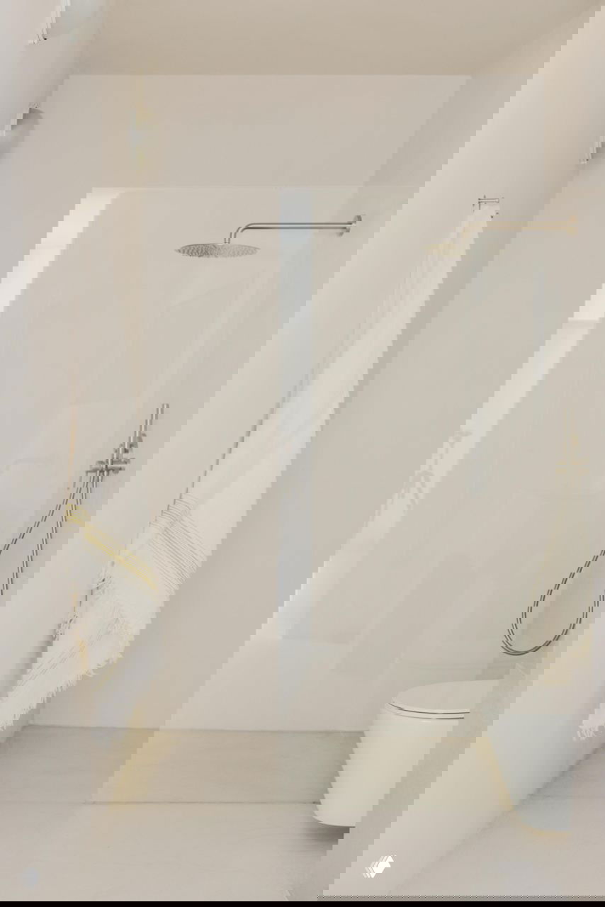 Светлая ванная с прозрачной стеклянной перегородкой душевой, простой напольный унитаз и текстиль на крючке в сдержанной палитре.